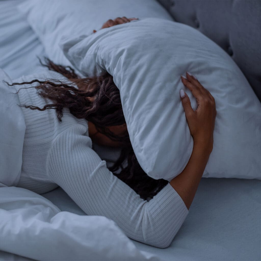 Woman struggling to fall asleep with pillow over her head — a common sign of poor sleep quality and nighttime overstimulation
