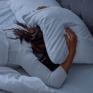 Woman struggling to fall asleep with pillow over her head — a common sign of poor sleep quality and nighttime overstimulation