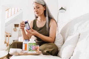 Woman in her 50s sitting on her couch reading a B-complex supplement label with a concerned expression, wondering if it's causing her anxiety