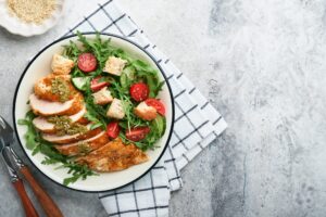 Person adding sliced chicken to a fresh salad — the balanced MTHFR diet approach combining plant foods with animal protein.