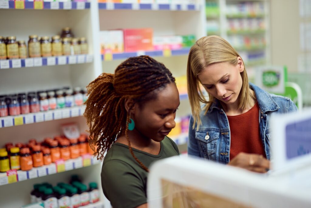 Store employee helping a customer compare B-vitamin supplement labels in the vitamin aisle.
