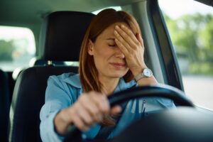 Woman stressed in a traffic jam — one everyday trigger of the chronic stress response that quietly wears your body down.
