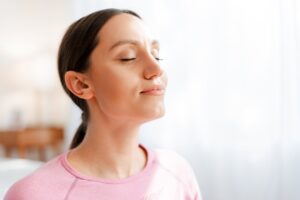 Woman doing breathing exercises with her eyes closed to calm her nervous system and reduce anxiety.