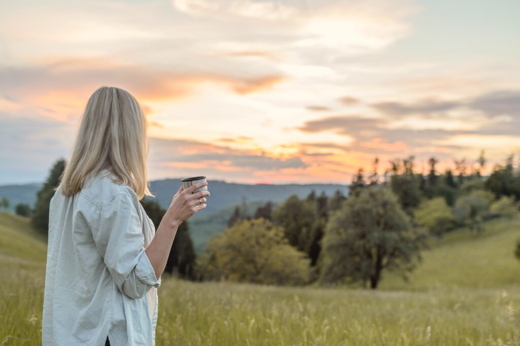 Woman walking in nature at sunrise with herbal tea — natural practices to calm the nervous system and reduce chronic stress