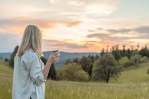 Woman walking in nature at sunrise with herbal tea — natural practices to calm the nervous system and reduce chronic stress